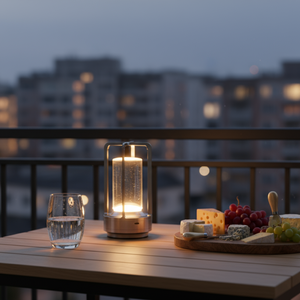 Dining table setup with candle lanterns, glasses, and food on a balcony at night.