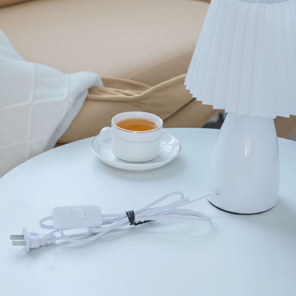White lamp on a table with a cup of tea and power cord in a cozy room setting.