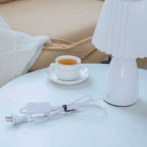White lamp on a table with a cup of tea and power cord in a cozy room setting.
