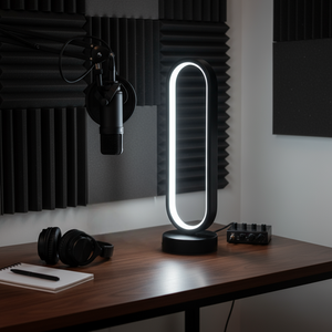 Modern desk lamp on a wooden surface with headphones and a microphone in a dark room.