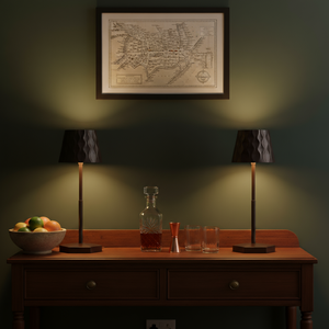 Wooden sideboard with fruit bowl, decanter, and glasses under two lamps against a wall with a framed map.