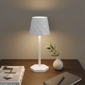 White table lamp on a table with a minimalistic setup including a plant and books.