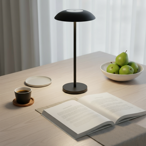Black table lamp on a wooden table with an open book, coffee cup, and bowl of apples.