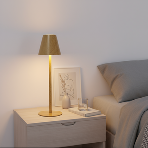 Gold table lamp on a nightstand next to a bed with a neutral color scheme.