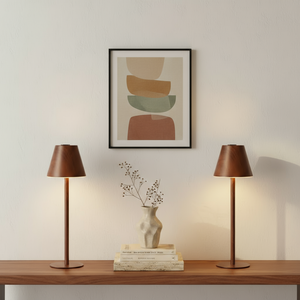 Modern desk setup with a lamp, notebook, pen, mug, and plant on a neutral background.