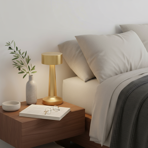 Gold lamp on a wooden nightstand next to a bed with gray bedding.