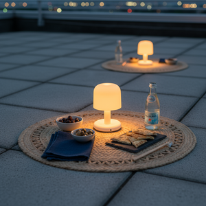 Outdoor setting with two small lamps, snacks, and a bottle on woven mats.