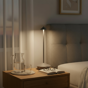 Bedroom scene with a nightstand, lamp, and books in a dimly lit room.