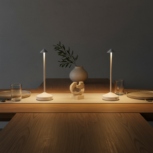 Two table lamps on a wooden surface with a vase and glasses in the background.