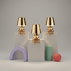 Three gold-colored lampshades on geometric platforms with colorful objects on a neutral background