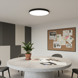 Modern office meeting room with round table, chairs, and a bulletin board on the wall.