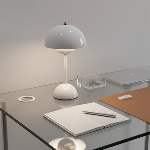 Modern desk setup with a white lamp, notebook, and pen on a glass surface.