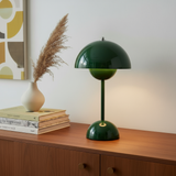 Green table lamp on a wooden surface with books and a vase in the background
