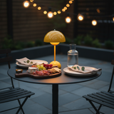 Outdoor setting with a small table featuring a cheeseboard, fruit, and a lamp under string lights.