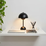 Black desk lamp on a white surface with a plant and stationery items.