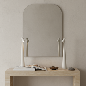Minimalist interior with a mirror, table, and decorative items against a plain wall.