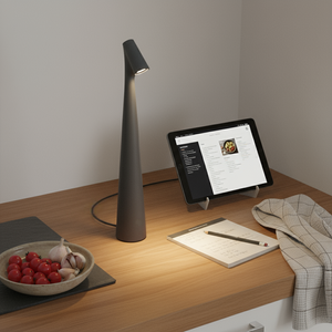 Desk setup with a modern lamp, tablet, and notepad on a wooden surface.