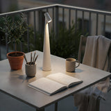 Table with a lamp, book, mug, and plant on a balcony at night.