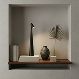 Modern shelf with a black lamp, books, and decorative items against a neutral wall.