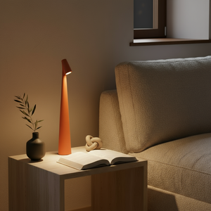 Orange lamp on a side table next to a book and small plant, with a sofa in the background.