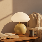 Yellow table lamp on a wooden side table with an open book and mug, in a cozy room setting.