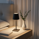 Lamp on a bedside table with a vase and plant in a bedroom setting