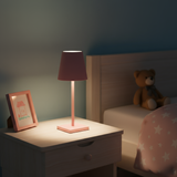 Pink lamp on a nightstand next to a teddy bear and framed picture in a bedroom setting.