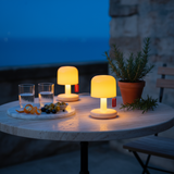 Two small table lamps on a marble table with glasses and snacks at night.