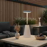Outdoor setting with a table, lamp, vase, and bowl in a garden or patio area.